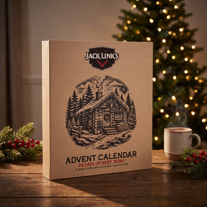 Jack Link's Advent Calendar on a wooden table with a lit Christmas tree, pine branches and a mug behind