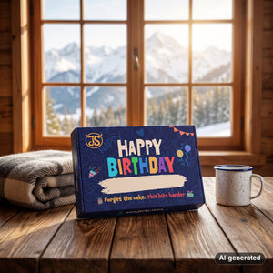 Happy Birthday Box on a wooden table in a mountain chalet, with a wool blanket, an enamel mug and snowy mountains outside, AI-generated image