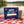 Happy Birthday Box on a checked picnic blanket by a lake on a summer day, with a steel cup and sunglasses, AI-generated image