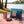 KoRo Freeze-Dried Strawberries in Milk Chocolate on a checked picnic blanket by a lake on a summer day, with a steel cup and sunglasses, AI-generated image
