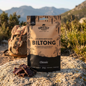 Grizzly Foods Biltong Classic 30g förpackning på en klippa vid vandringsled, biltongskivor och ryggsäck bakom